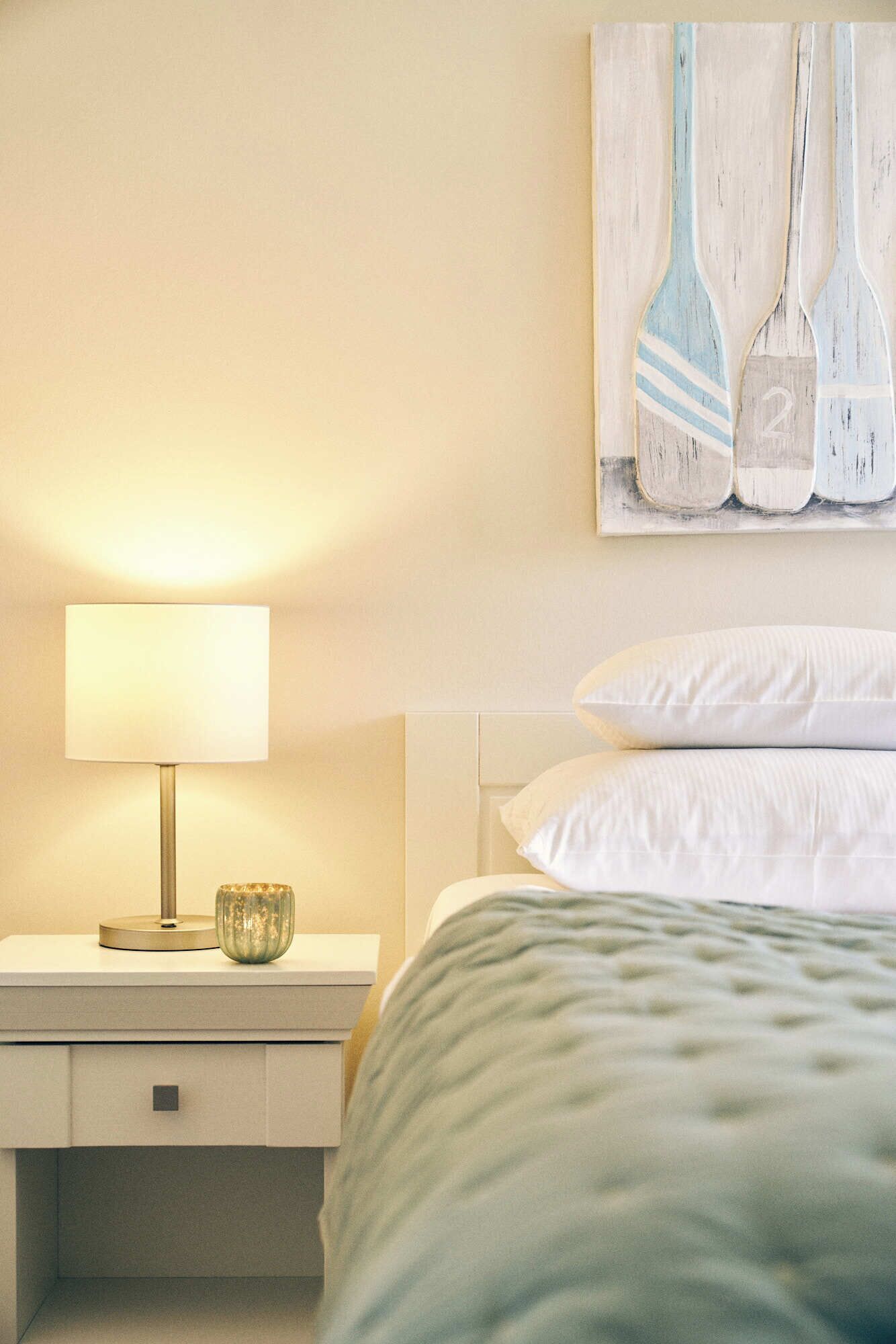 A neatly made bed with white pillows, a bedside lamp, and a small decorative bowl on a bedside table.