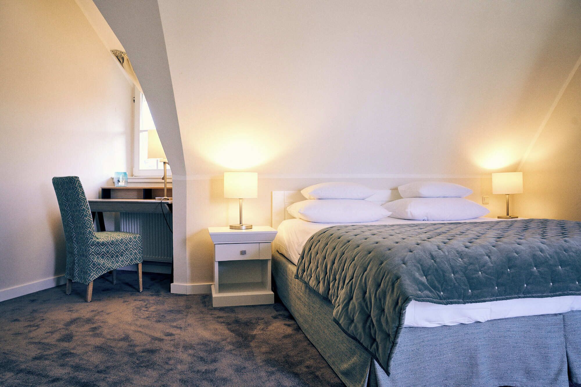 Een hotelkamer met een bed, twee bedlampen, een bureau met stoel en een spiegel.