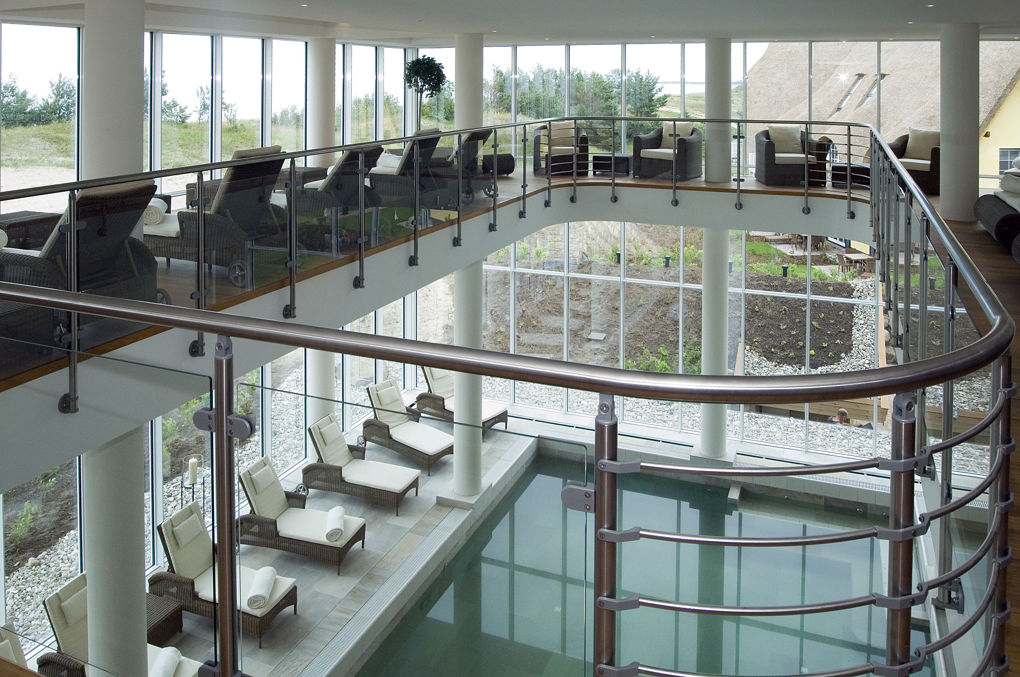 Ein moderner Poolbereich im Innenbereich mit Glasgeländern, Liegestühlen und Blick auf die umliegende Landschaft.