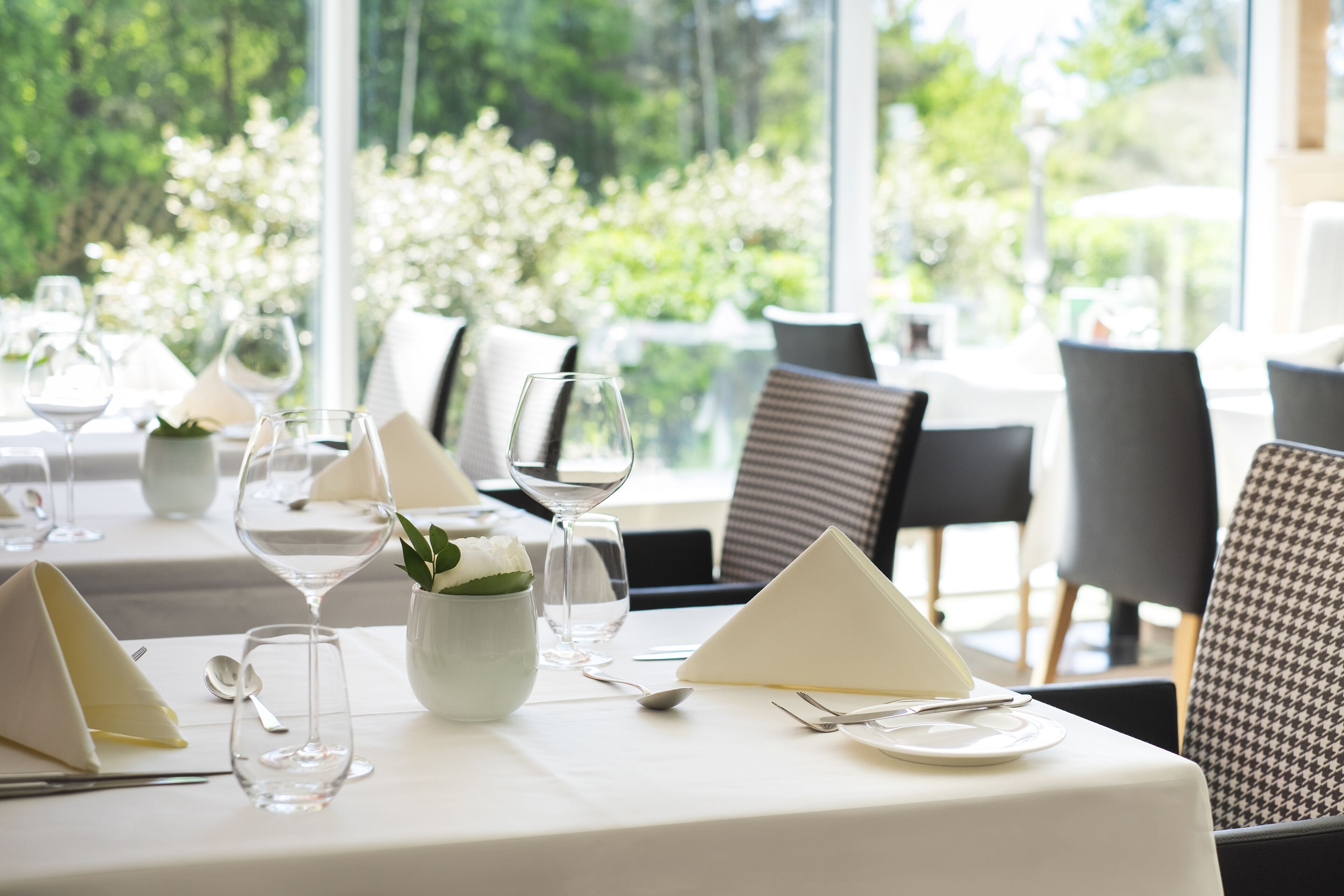 Une table à manger dressée avec une nappe blanche, de la verrerie et un vase rempli de fleurs.