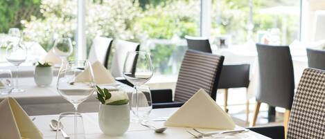 Une table à manger dressée avec une nappe blanche, de la verrerie et un vase rempli de fleurs.