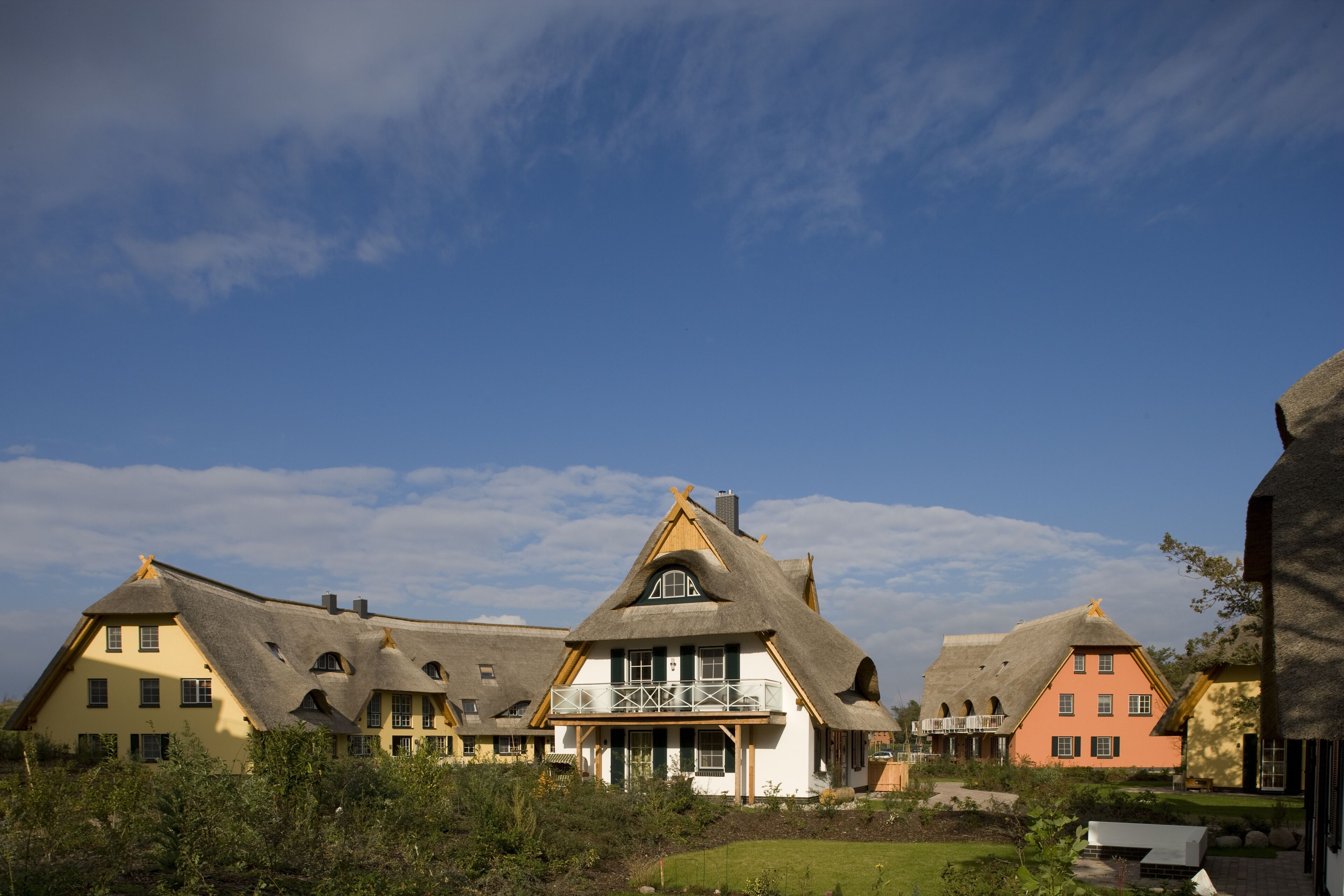 A row of traditional houses with thatched roofs, a central building with a balcony, and a well-maintained garden.