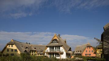 A row of traditional houses with thatched roofs, a central building with a balcony, and a well-maintained garden.