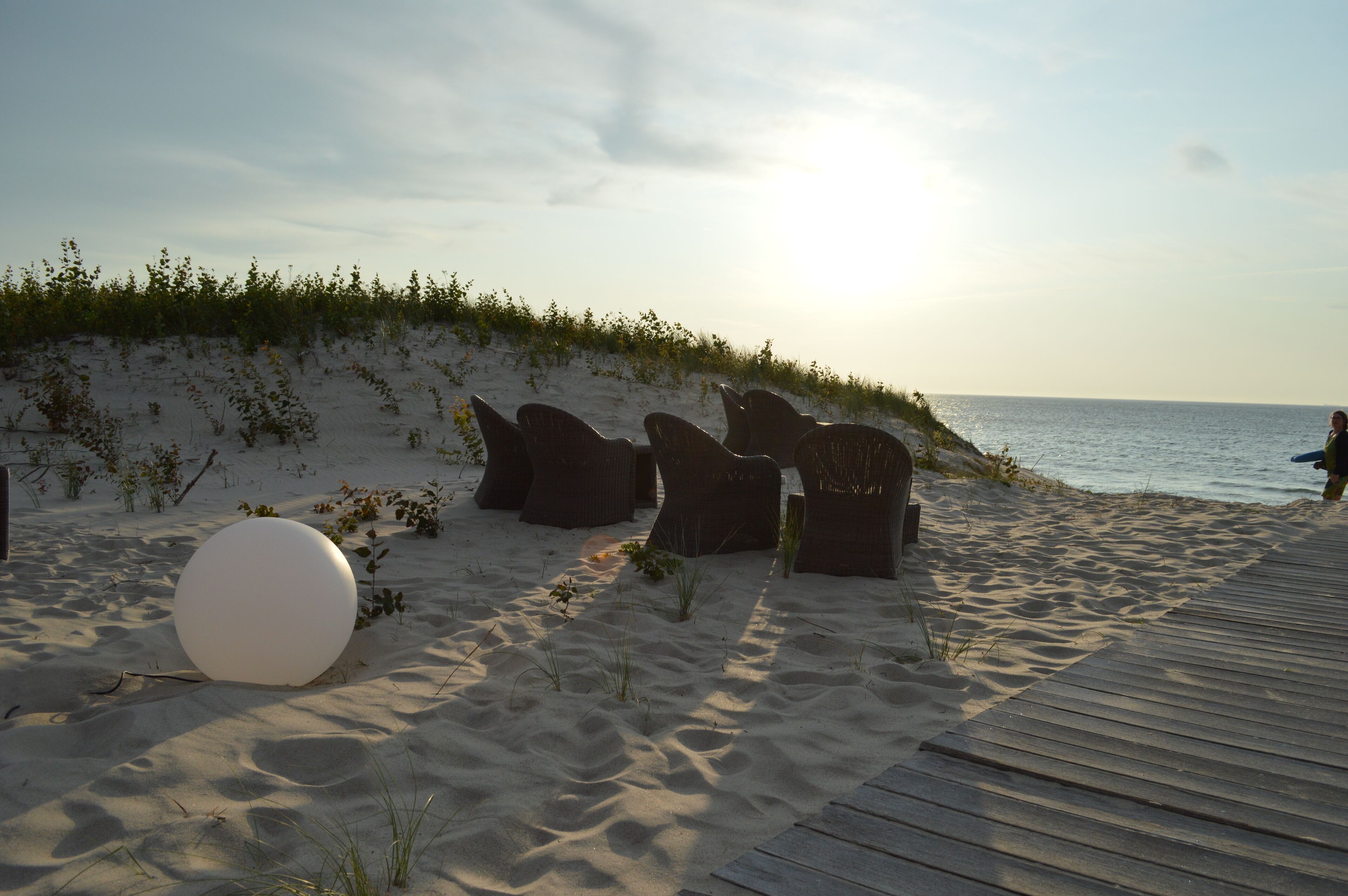A beachside area with a wooden deck, wicker chairs, and a large white sphere.