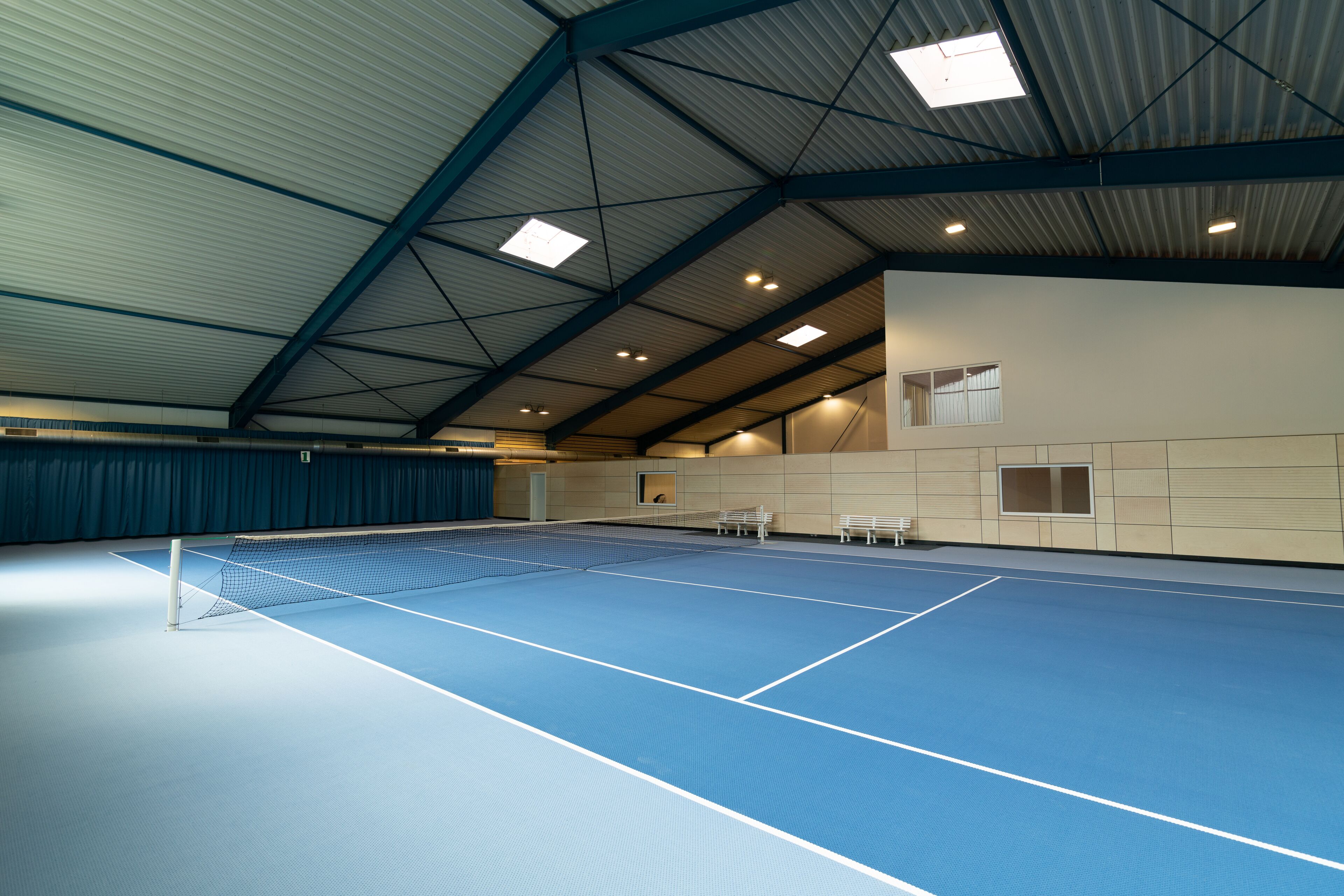 An indoor tennis court with a high ceiling and multiple windows.