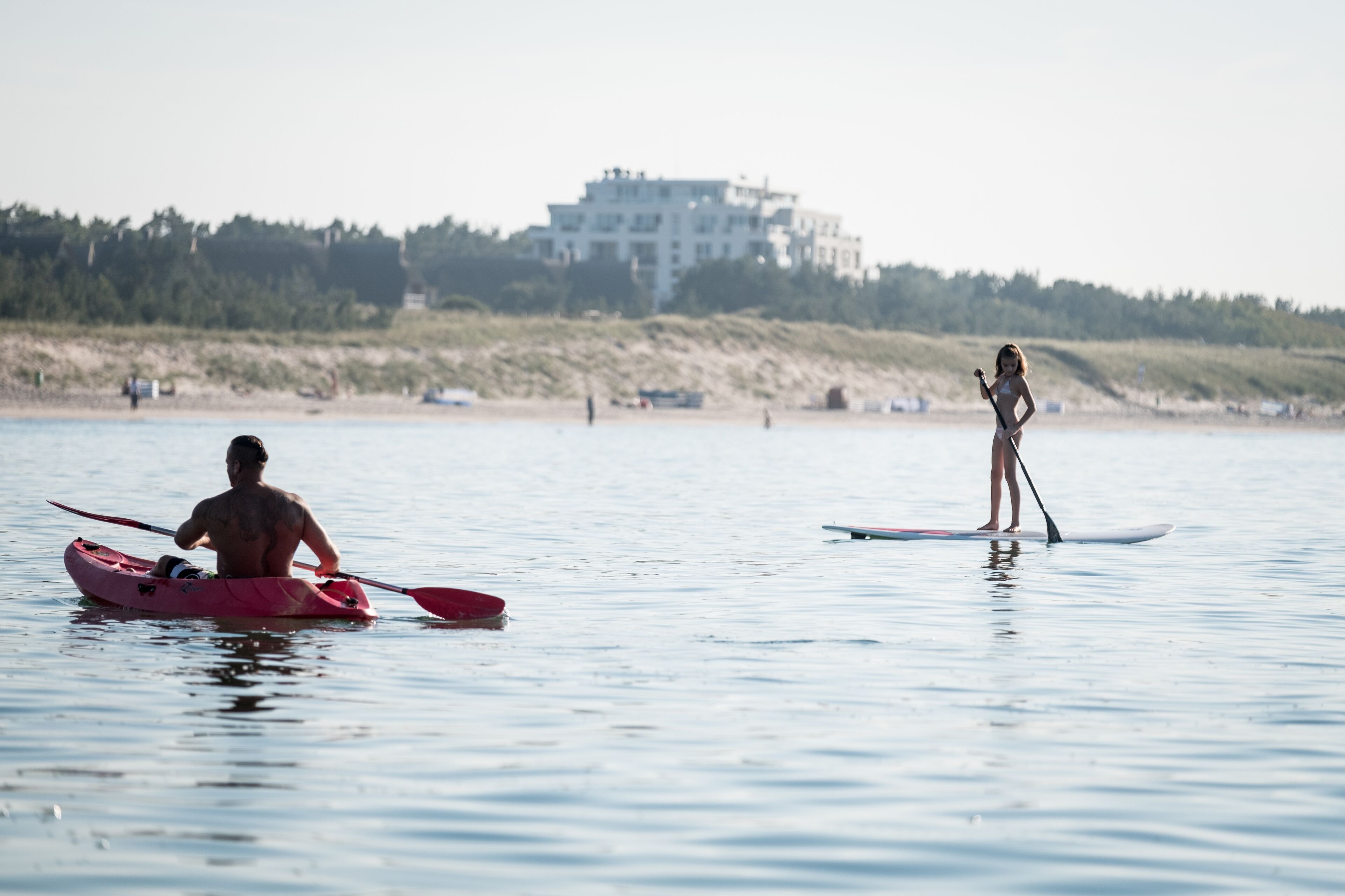 A beach scene with a person kayaking and another standing on a paddleboard.
