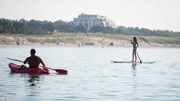 A beach scene with a person kayaking and another standing on a paddleboard.