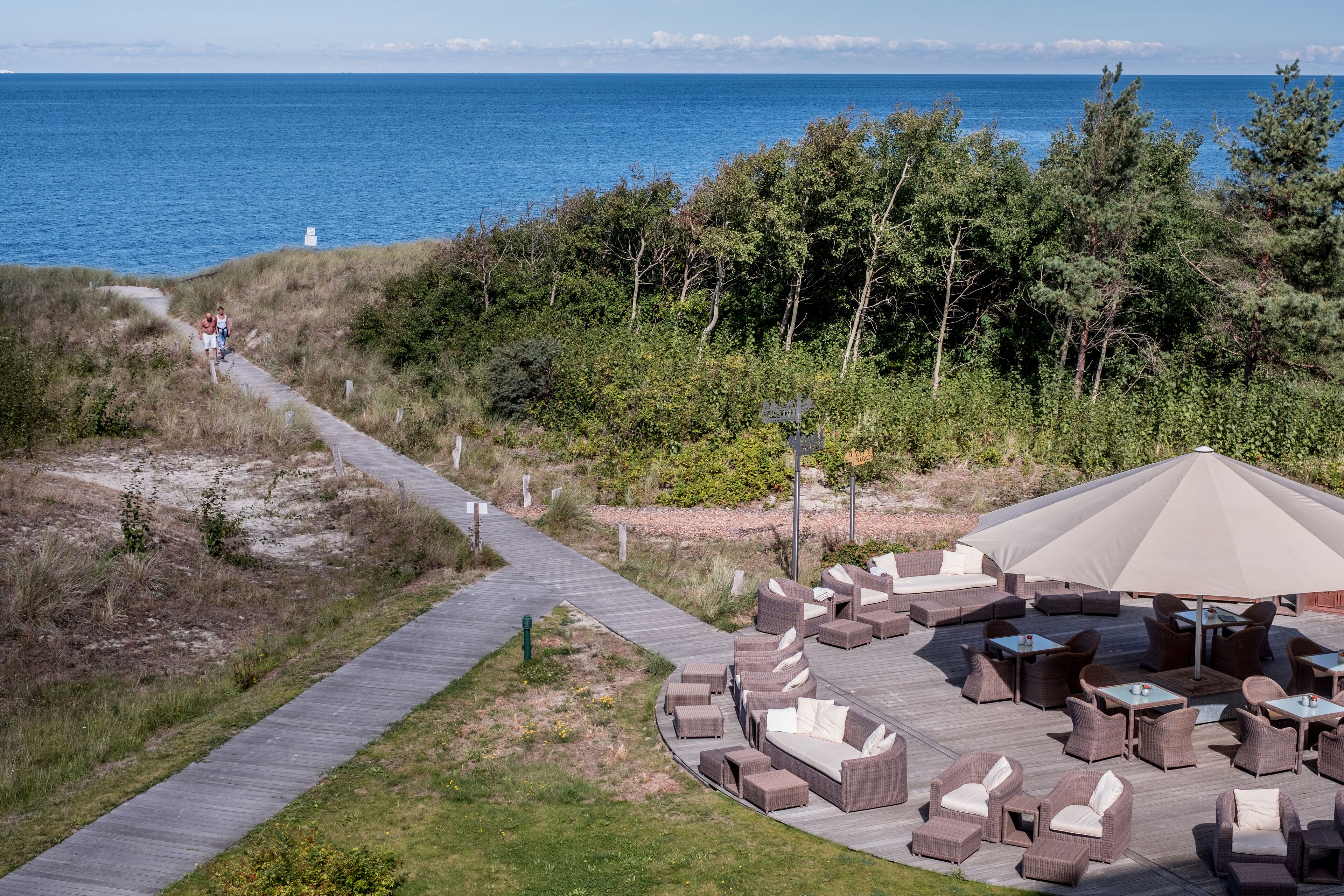A coastal outdoor seating area with a view of the sea, a wooden deck, and lounge furniture.