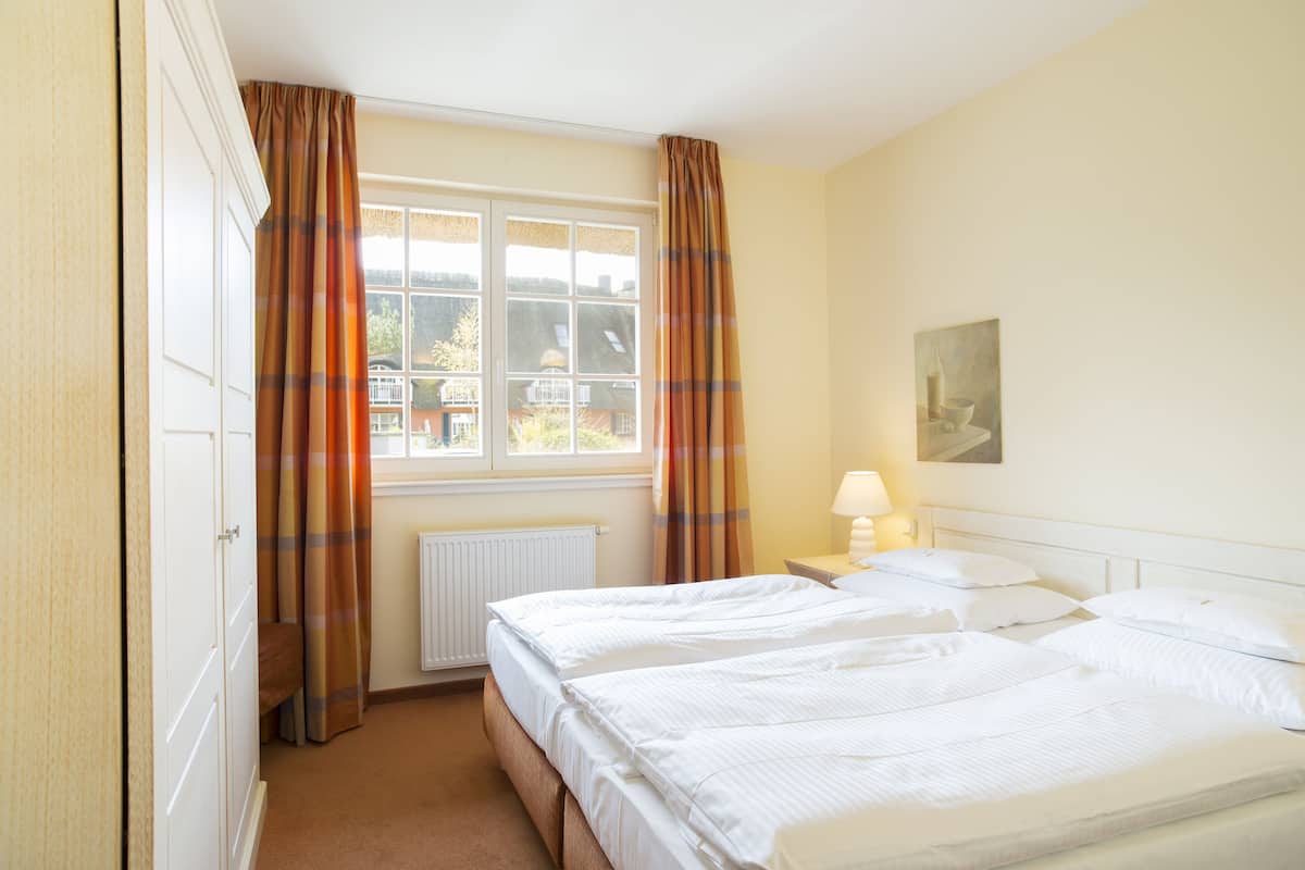 A hotel room with two beds, a window with curtains, a radiator, and a painting on the wall.