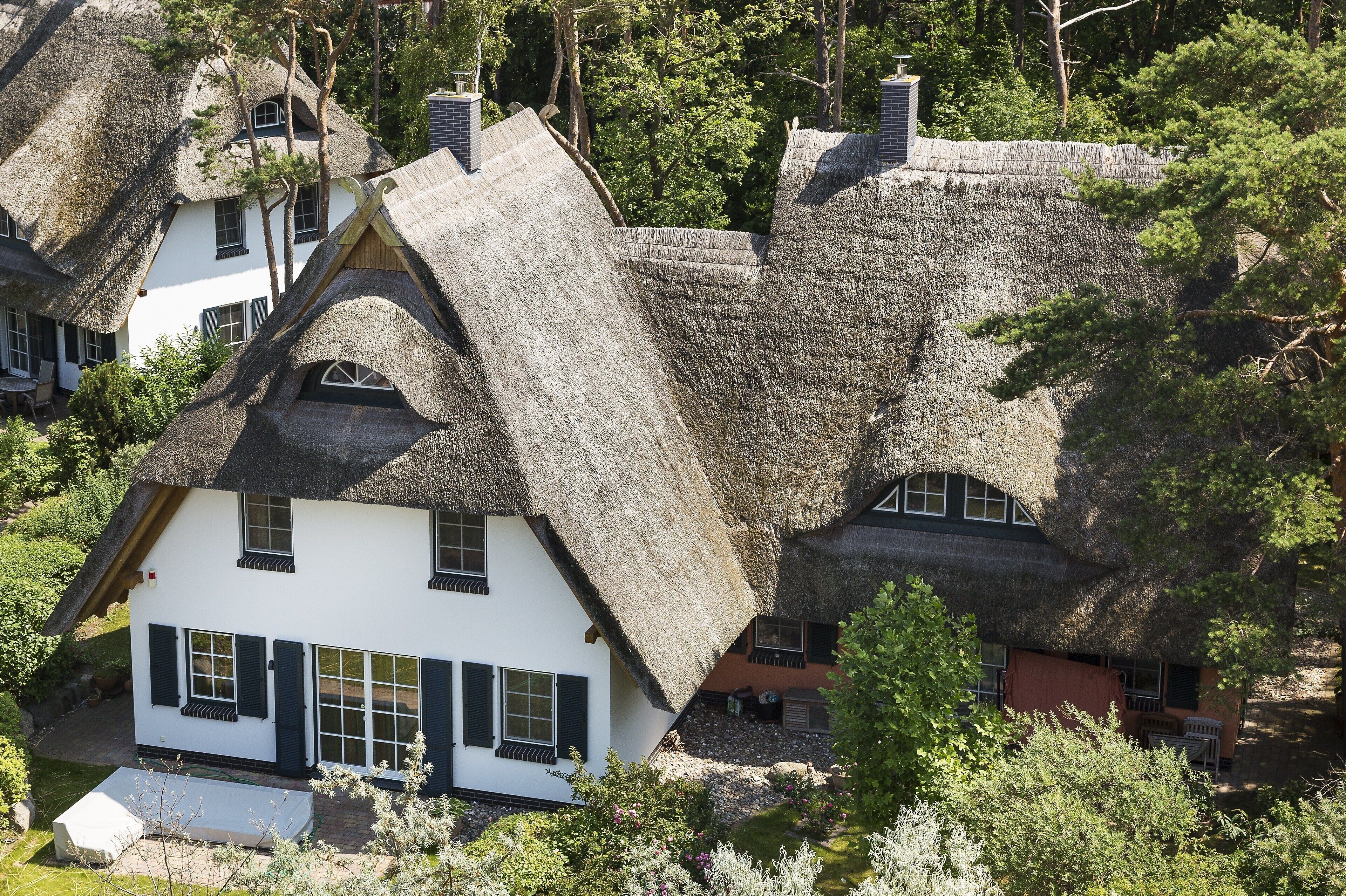 A traditional house with a steeply pitched thatched roof and white walls, surrounded by trees.