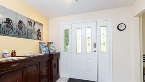 Uma área de recepção com uma mesa de madeira, um quadro, uma porta dupla com painéis de vidro e um relógio na parede.