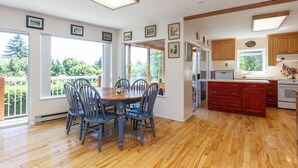 Cozinha espaçosa com piso de madeira, área de refeições com mesa e cadeiras, e janelas amplas com vista para o verde.