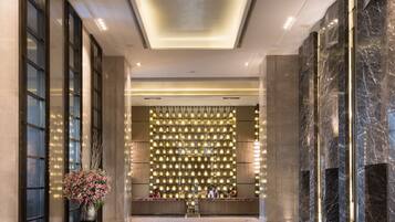 A modern hotel lobby with a marble floor, a patterned rug, and a decorative wall with lights.