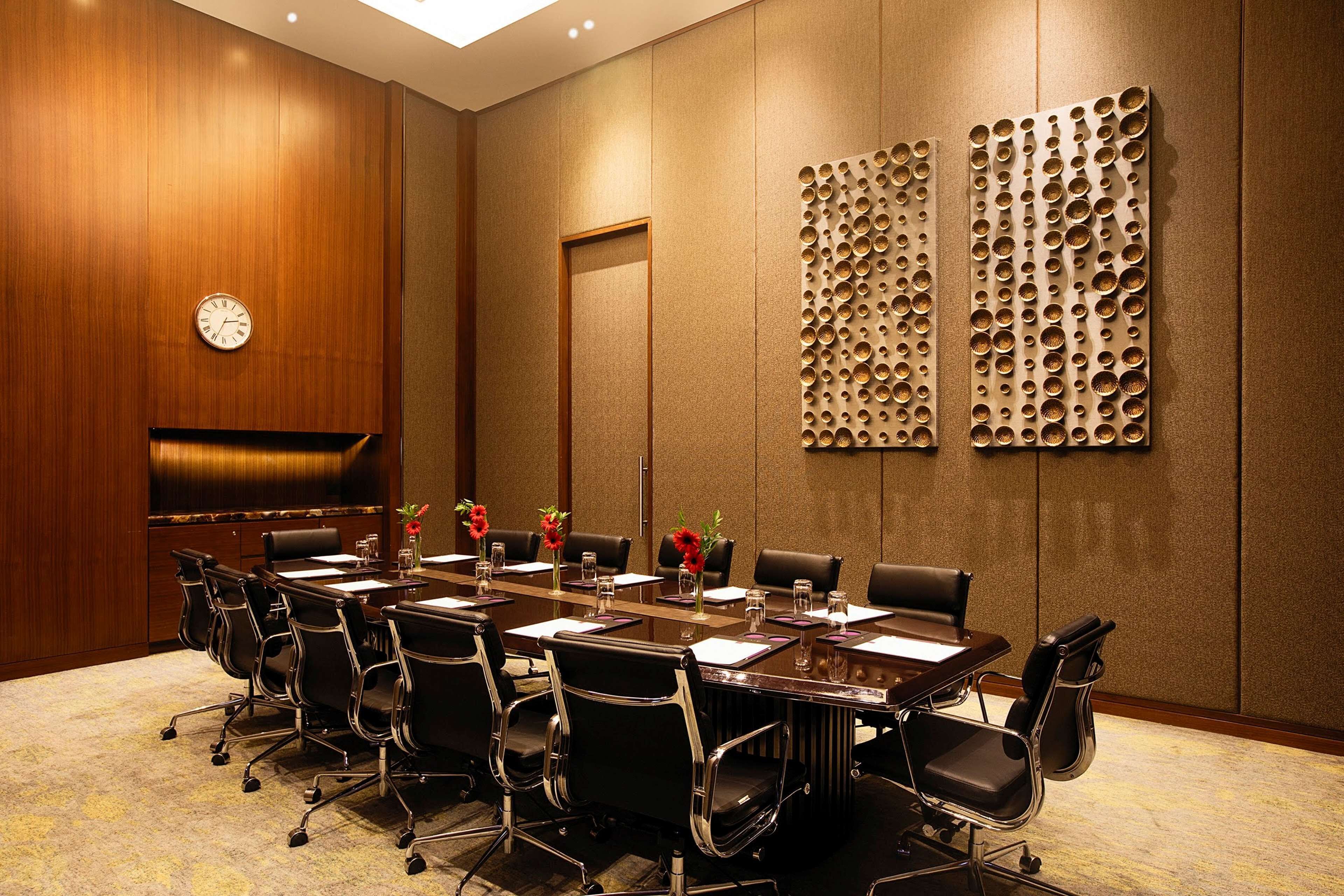 Un salón de conferencias con una larga mesa, sillas, un reloj y paneles decorativos en la pared.