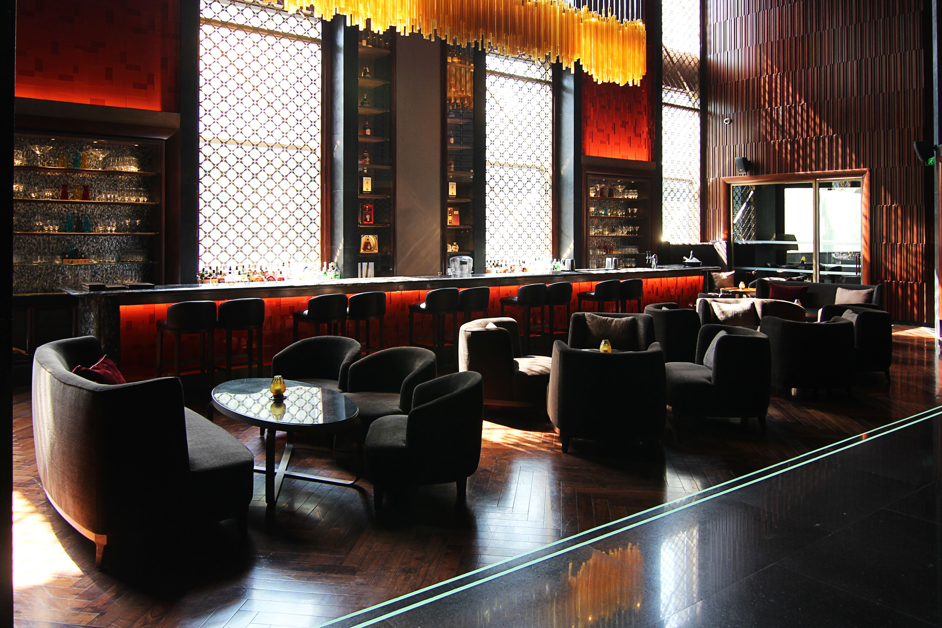 A modern bar area with seating, a bar counter, and a large window with patterned curtains.