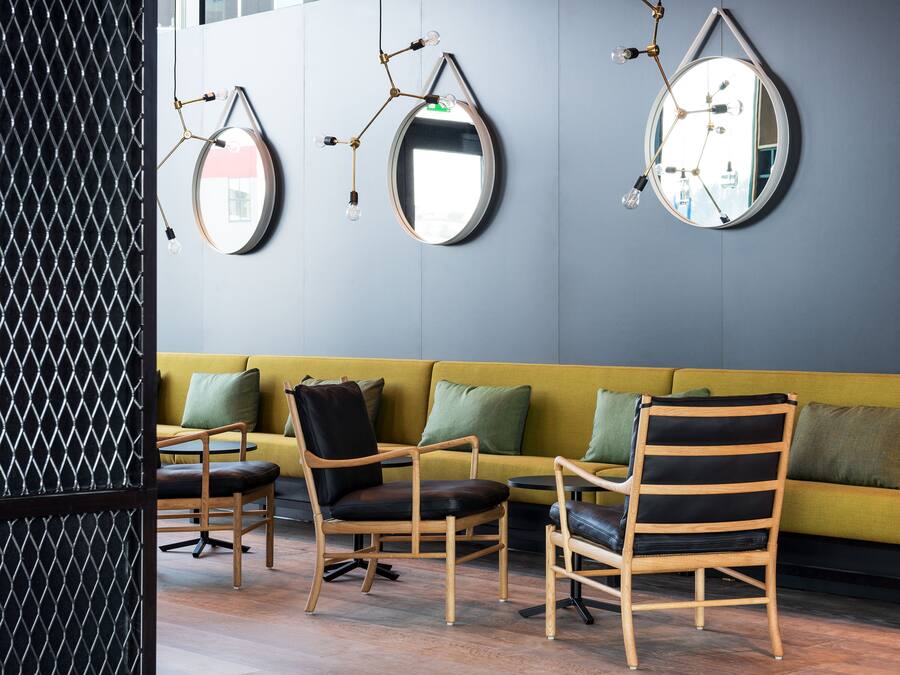 A modern interior with a yellow sofa, wooden chairs, and three wall-mounted mirrors.