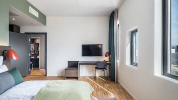 Een moderne hotelkamer met een bed, bureau, stoel, televisie en grote ramen.