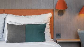 Una cama bien hecha con varios almohadones, un cabecero de madera, una mesita de noche con lámpara y un enchufe.