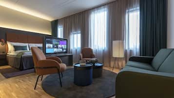 A modern hotel room with a bed, a TV, a sofa, a coffee table, and a floor lamp.