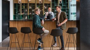 A bar area with wooden stools, a bar counter, and shelves stocked with bottles and glasses. - Quality Hotel Pond (Sandnes)