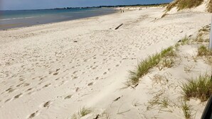 A sandy beach with footprints and sparse grass, a clear sky, and a distant shoreline. - Quality Hotel Pond (Sandnes)