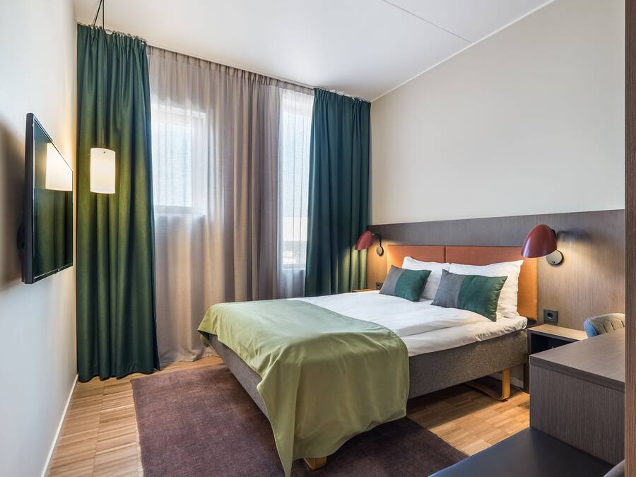 Ein modernes Hotelzimmer mit Bett, Schreibtisch und einem an der Wand befestigten Fernseher.