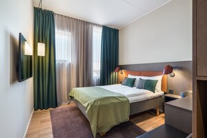 A modern hotel room with a bed, a desk, and a TV mounted on the wall.