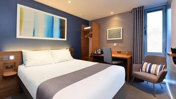 A hotel room with a large bed, a desk, a chair, a wardrobe, and a painting on the wall.