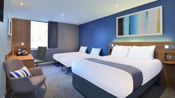 Habitación de hotel con dos camas, un escritorio, una silla y un cuadro abstracto grande en la pared.