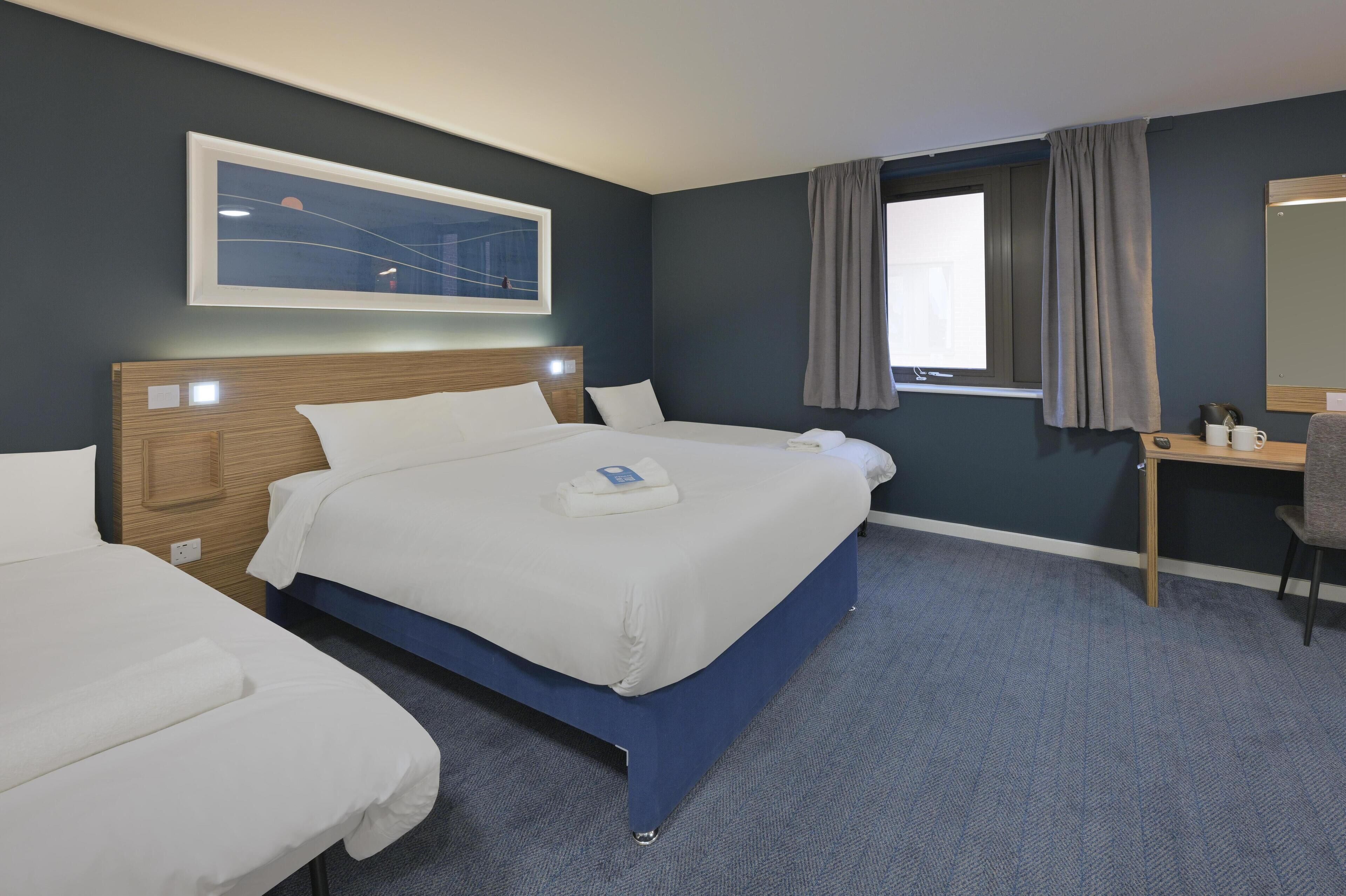 Habitación de hotel con dos camas, un escritorio, una silla, un ventanal con cortinas y un cuadro en la pared.