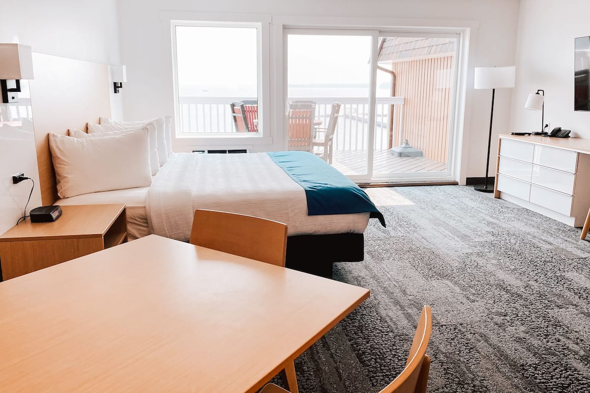 Quarto de hotel com cama, escrivaninha, cadeira, cômoda e televisão.