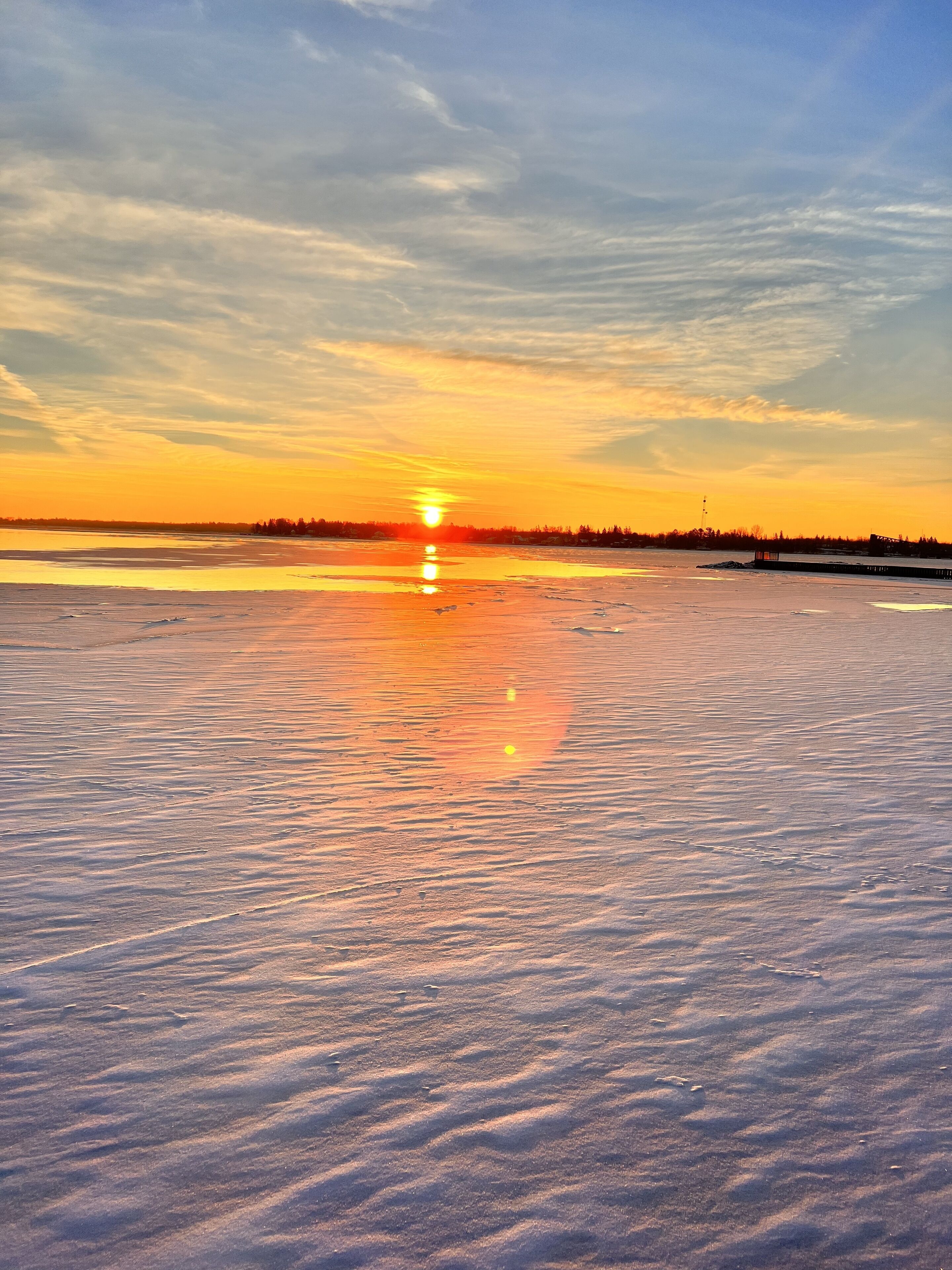 Un paisaje helado con un atardecer sobre una masa de agua.