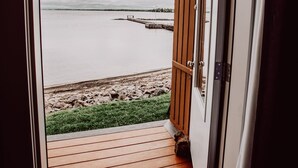 An open door leading to a wooden deck with a view of a calm body of water and a pier.