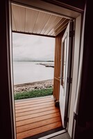 Puerta abierta que da a una terraza de madera con vista a un cuerpo de agua tranquilo y un muelle.