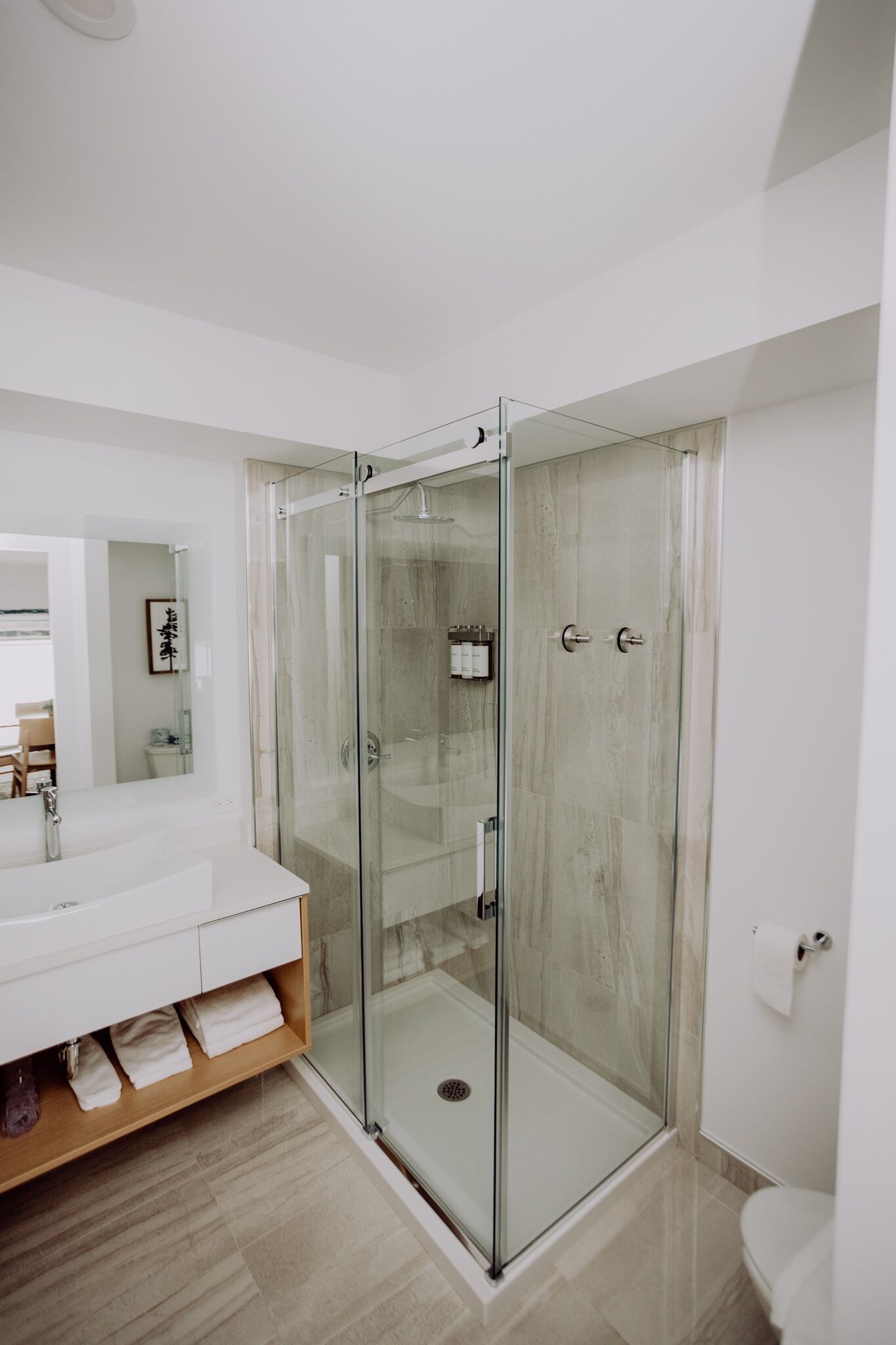 Un bany modern amb dutxa envidriada, un lavabo blanc i un armari de tocador de fusta.