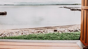 A wooden deck leading to a beach with a view of calm water and a distant pier.