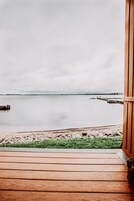 Una terraza de madera que conduce a una playa, con vista a aguas tranquilas y un muelle distante.