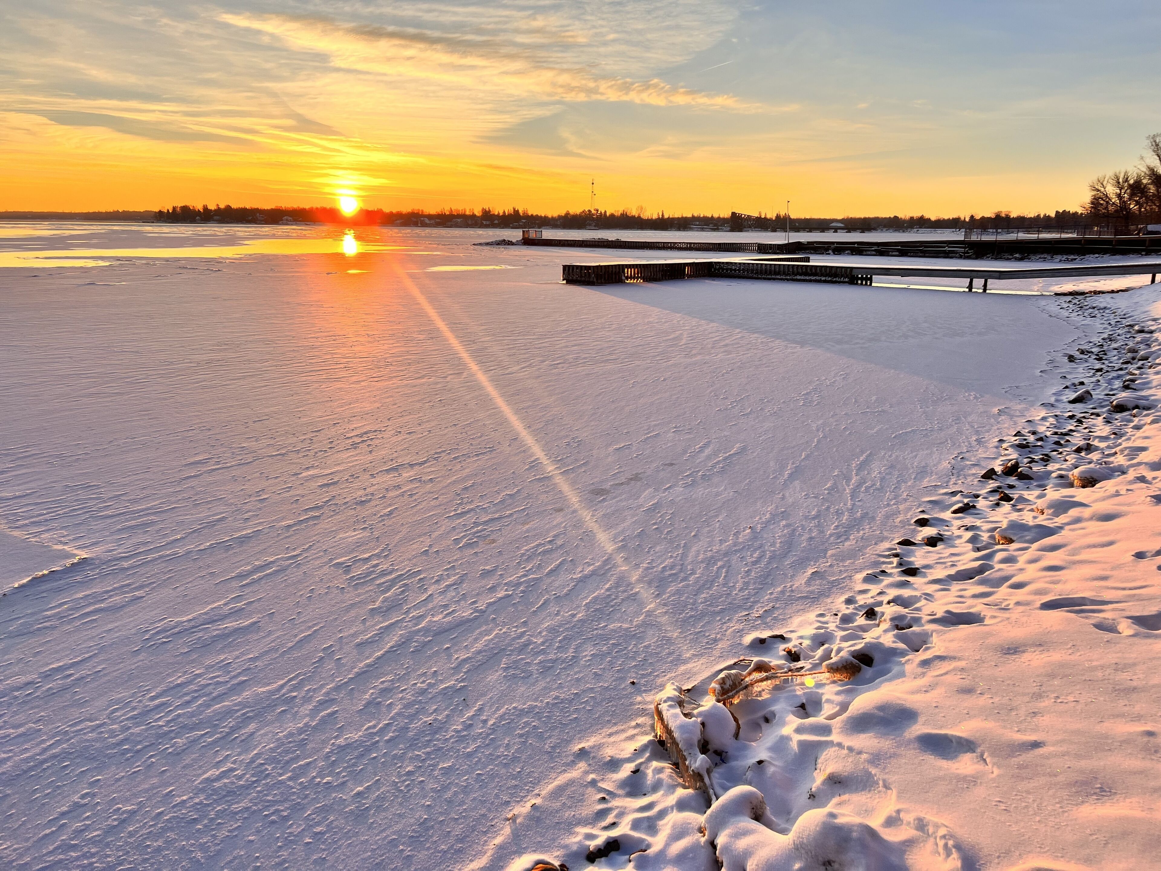 A frozen lake with a wooden dock extending into the water, surrounded by snow-covered land.