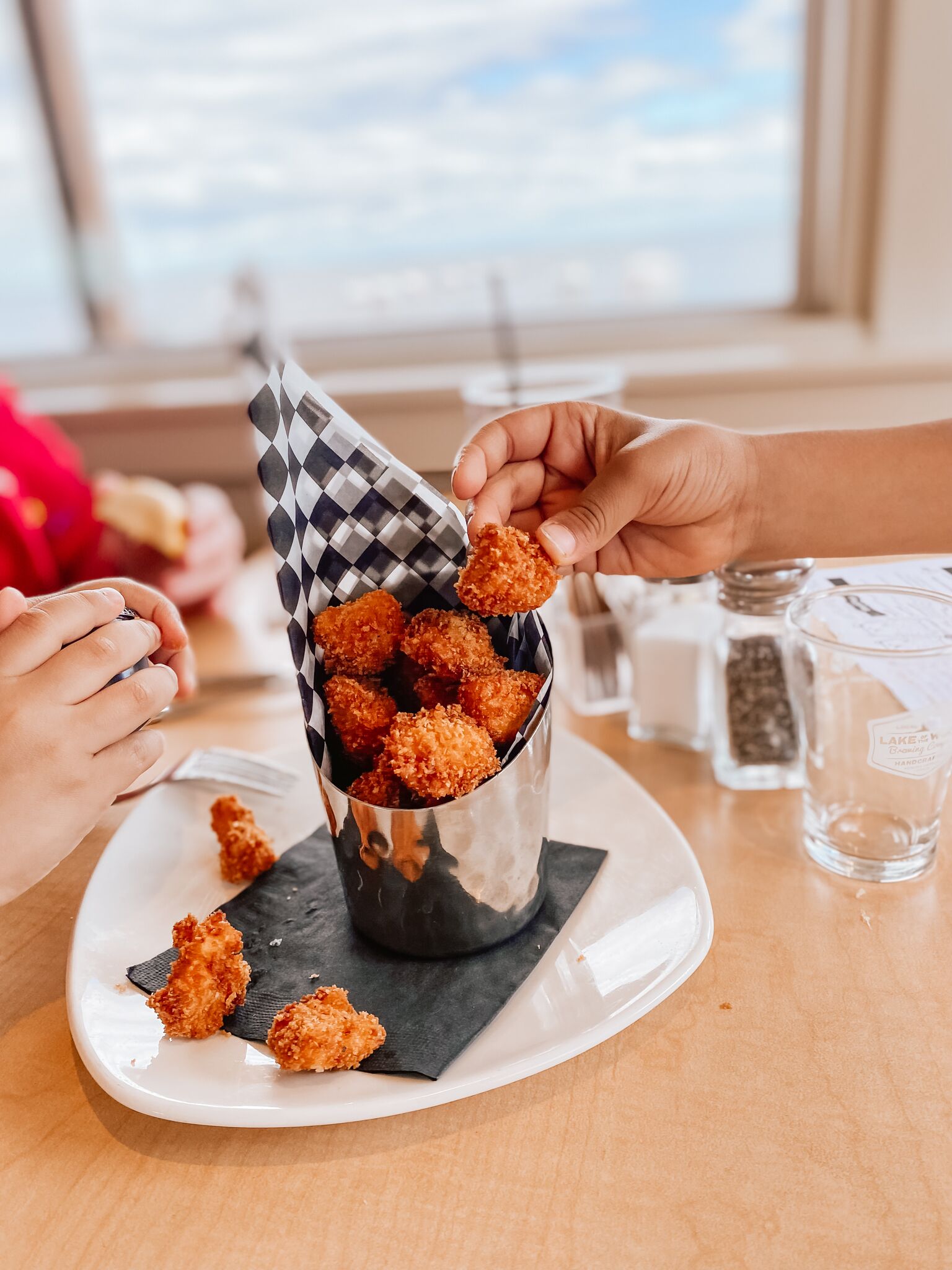 Une tasse en métal remplie d’aliments frits, posée sur une assiette blanche, avec une serviette à carreaux en dessous.