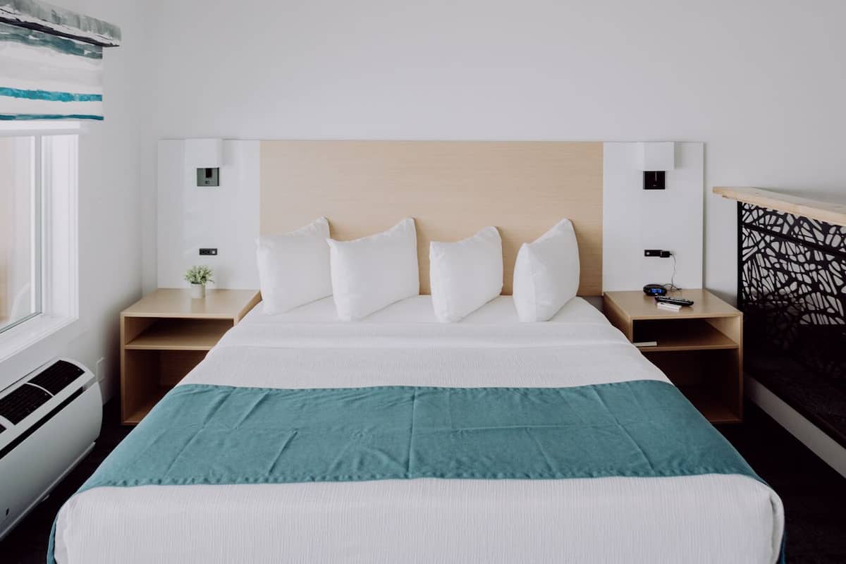 Quarto de hotel com uma cama grande, duas mesas de cabeceira, uma janela com vista e ar condicionado fixado na parede.
