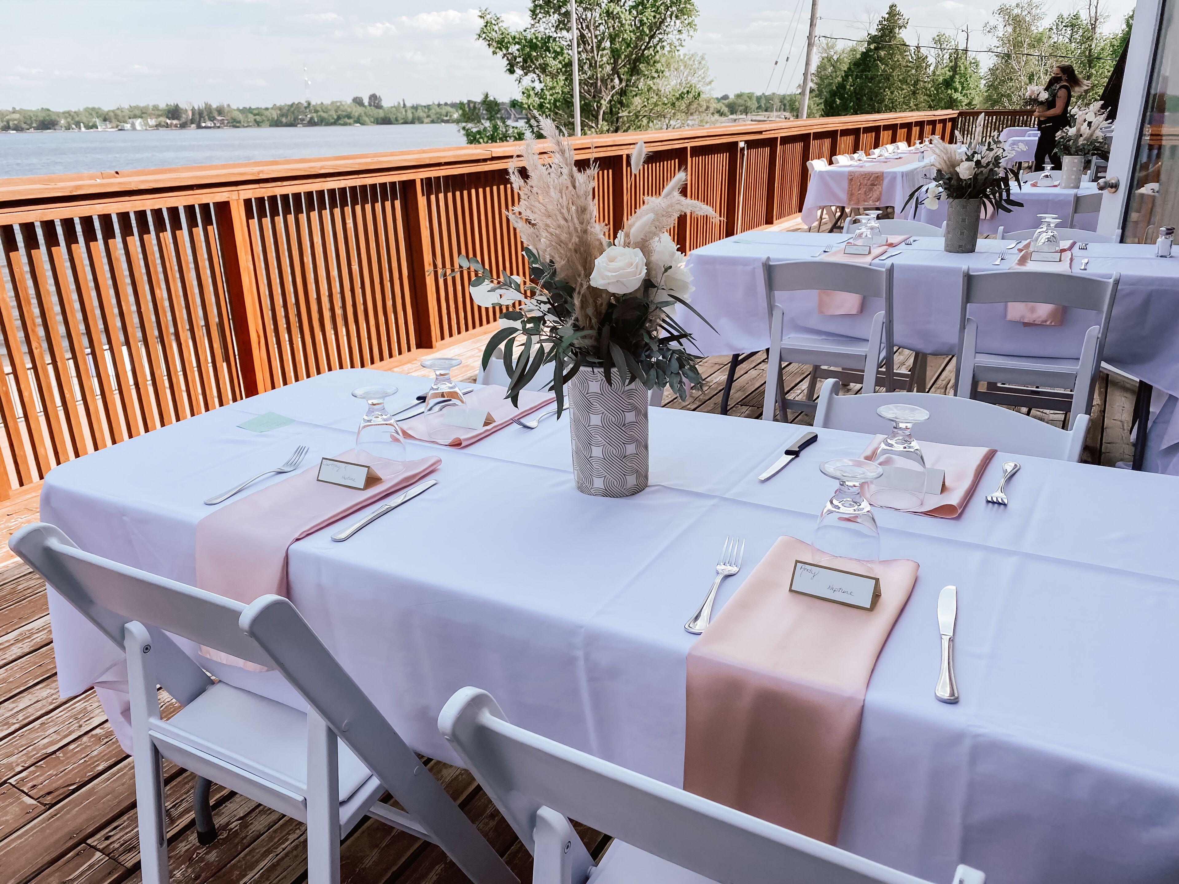 An outdoor dining area with tables set for a meal, overlooking a body of water.