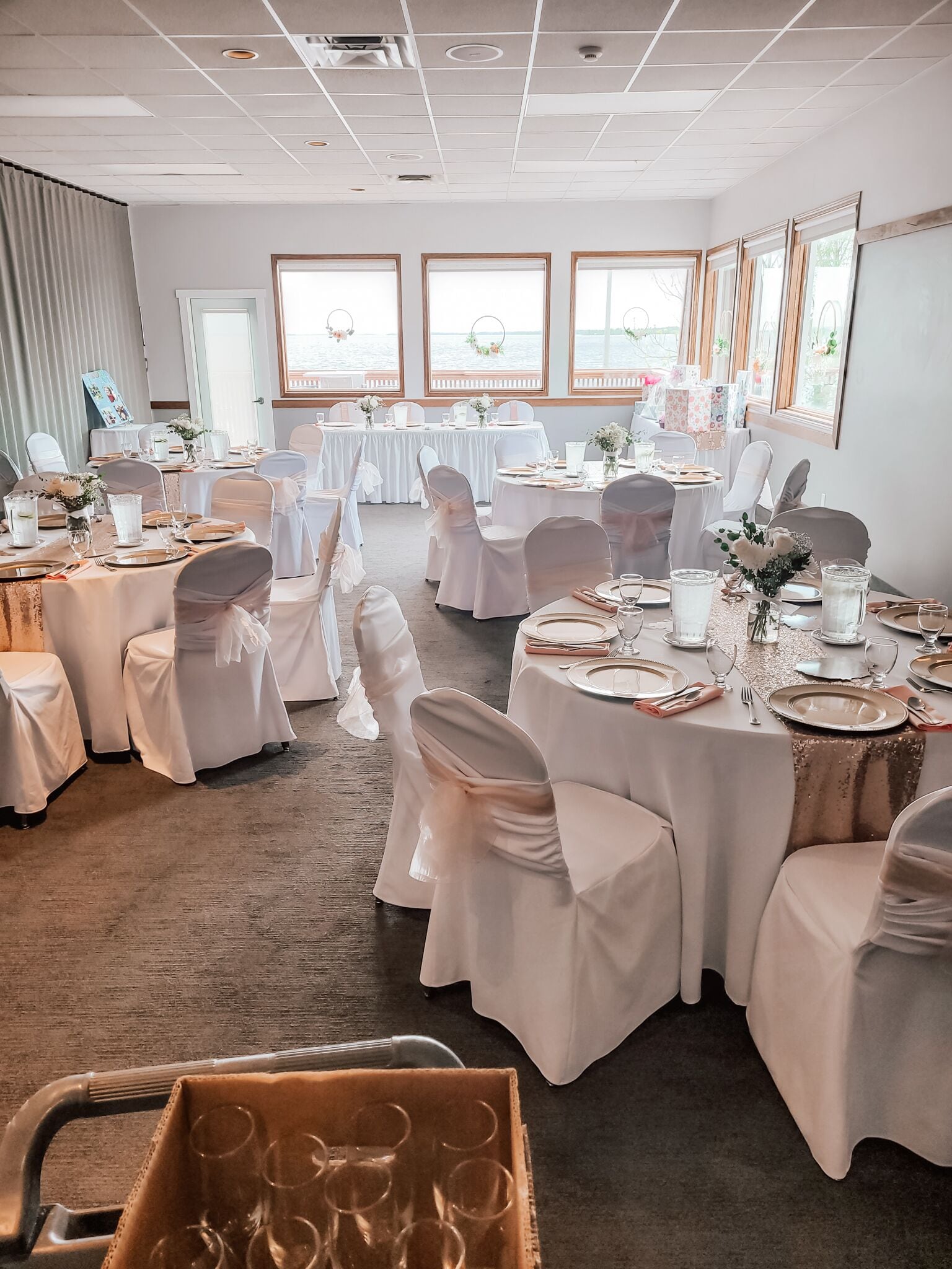 Une salle de banquet avec des tables rondes dressées pour un événement formel, agrémentée de nappes blanches et de chaises ornées de rubans blancs.