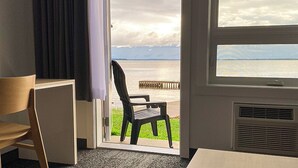 A room with a view of a body of water, a wooden chair, and a table.
