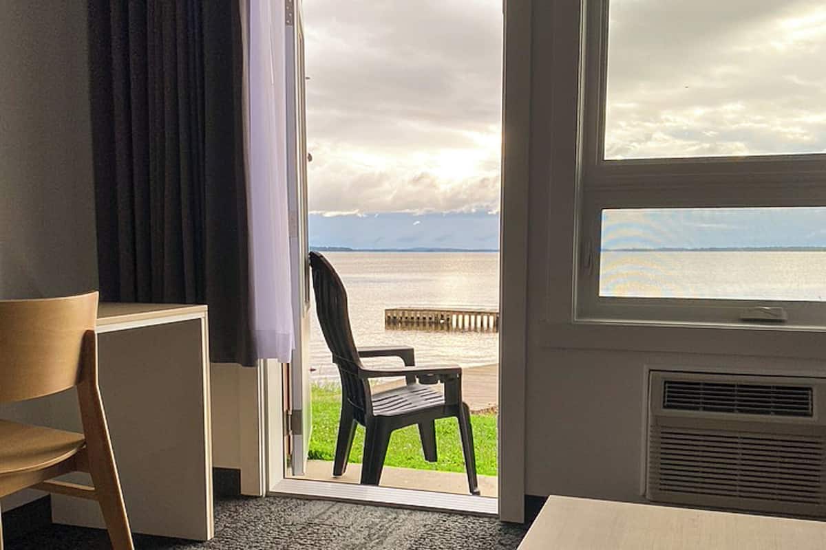 Quarto com vista para um corpo d'água, uma cadeira de madeira e uma mesa.