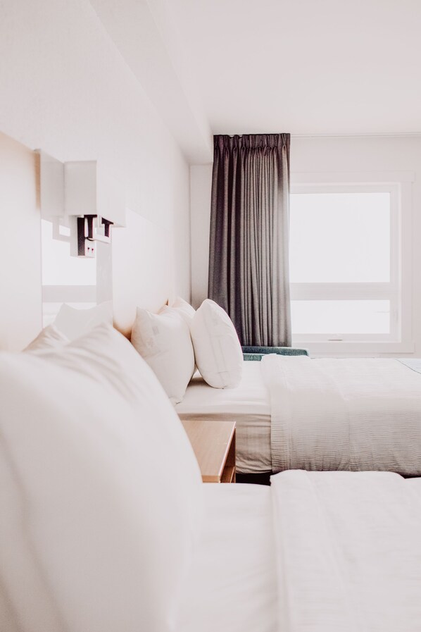 A hotel room with a large bed, a bedside table, a window with curtains, and a mirror on the wall. - La Place Rendez-Vous (Fort Frances)