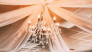 A banquet hall with a large chandelier, draped fabric ceiling, and tables set for a formal event.