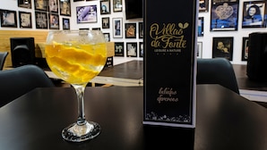 A table with a glass of yellow beverage and a black box with gold text. - Villas da Fonte Leisure and Nature (Leiria)