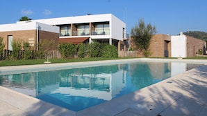 A modern pool area with a rectangular pool, surrounded by a wooden deck and a low brick wall. - Villas da Fonte Leisure and Nature (Leiria)