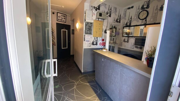 Een hotel lobby met een receptiebalie, een wandklok en een plattegrond.