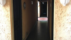 Un pasillo con piso de baldosas, techo de madera y paredes en color claro.
